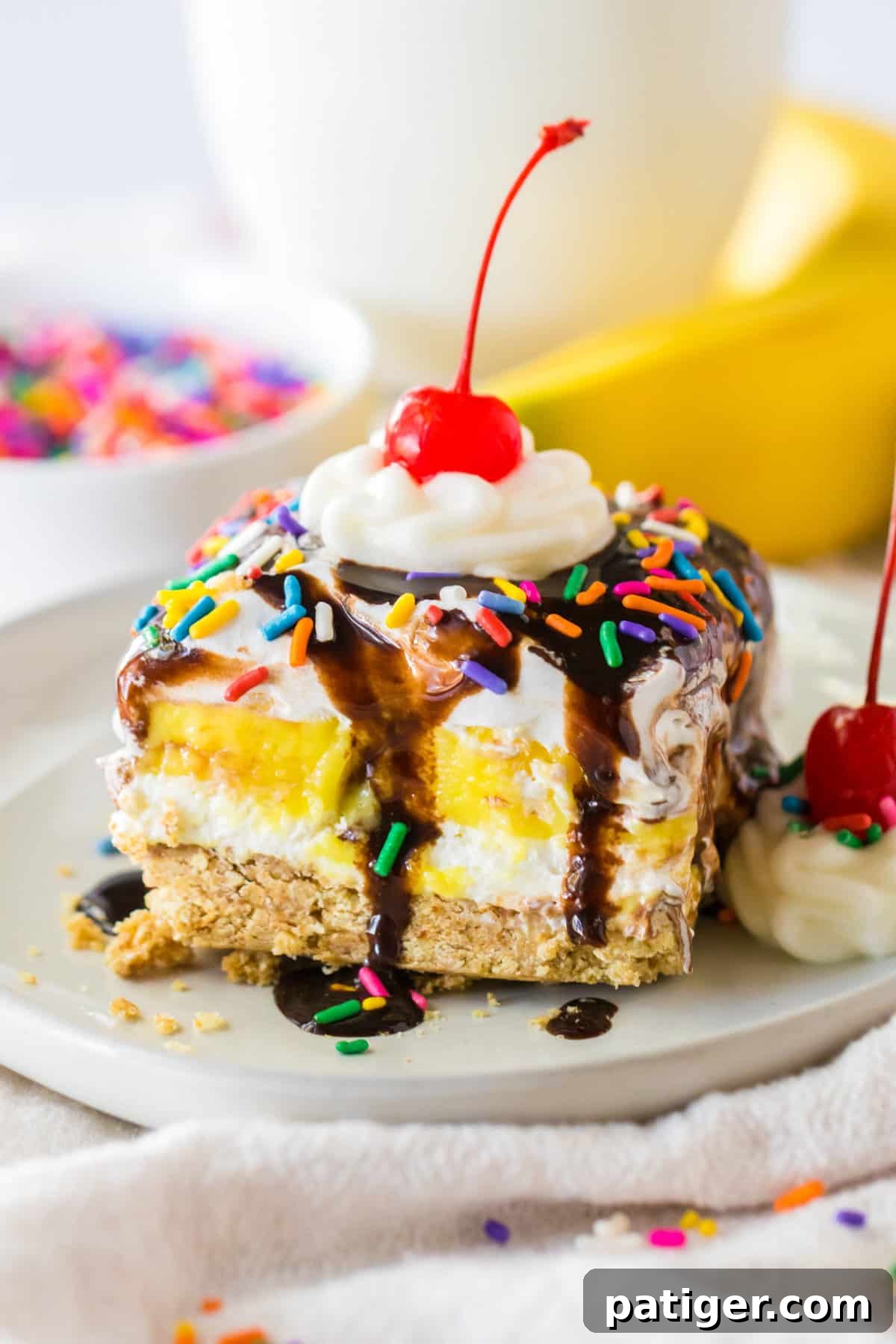 No bake banana split dessert with a graham cracker crust; layers of sweetened cream cheese, banana pudding, and Cool Whip; and topped with chocolate syrup, whipped cream, and a cherry.