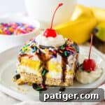 No bake banana split dessert with a graham cracker crust; layers of sweetened cream cheese, banana pudding, and Cool Whip; and topped with chocolate syrup, whipped cream, and a cherry.