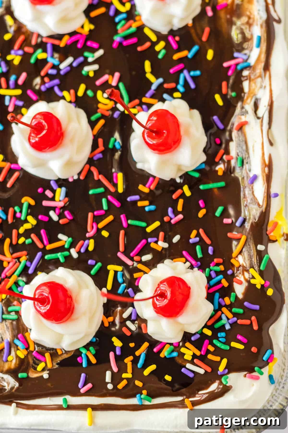 Banana split lush dessert with chocolate sauce, sprinkles, whipped cream, and cherries on top.