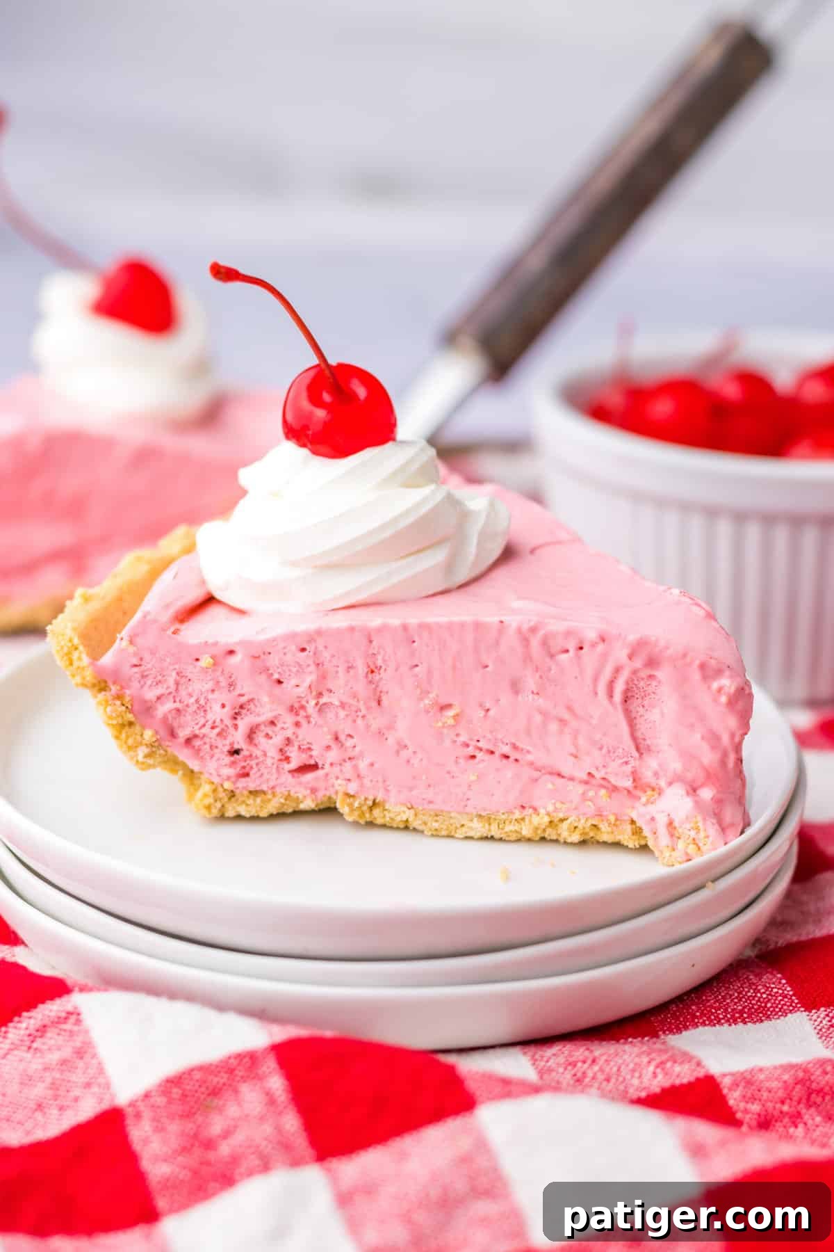 Summer Sip Pie 2 A perfectly sliced piece of no-bake Kool-Aid pie, adorned with a dollop of whipped cream and a bright red maraschino cherry on top, ready to be enjoyed.