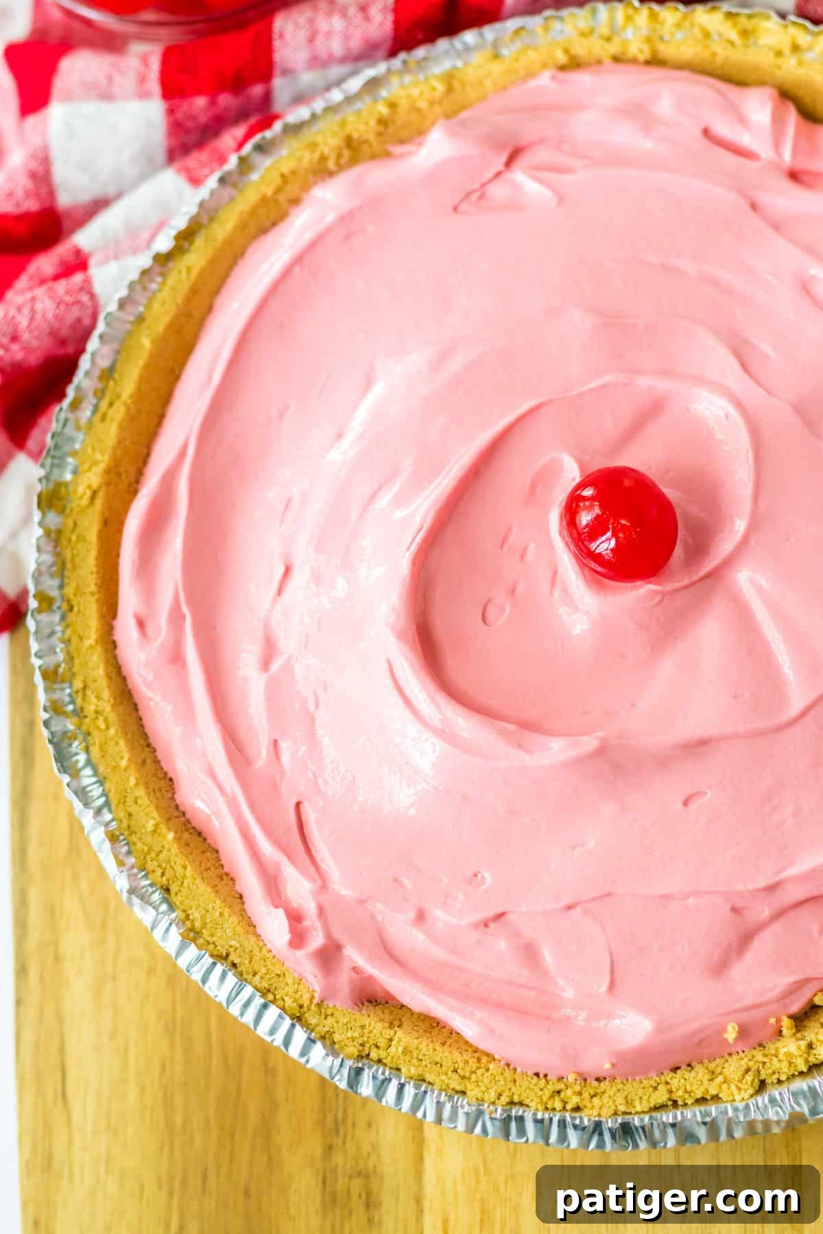 Summer Sip Pie 3 An overhead shot showcasing a beautiful pink, creamy no-bake Kool-Aid pie nestled in a golden graham cracker crust, with a glistening maraschino cherry at its center.