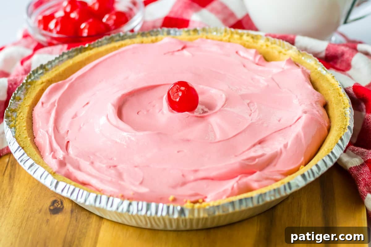 Summer Sip Pie 8 A beautiful cherry Kool-Aid pie, complete with a dollop of whipped cream, resting in a golden graham cracker crust, showcasing the final ready-to-serve dessert.