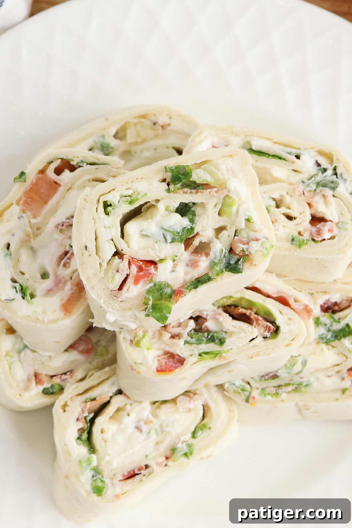 Overhead photo of ranch blt pinwheels stacked on top of one another and served on a white plate. These vibrant tortilla roll-ups feature layers of crispy bacon, fresh lettuce, and bright red tomatoes, all held together with a creamy ranch spread, making them an ideal appetizer for any occasion.