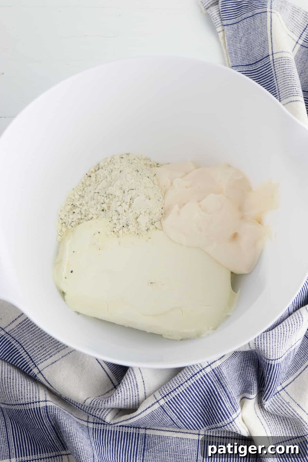 Ranch mix, cream cheese, and mayo in mixing bowl. The three ingredients are ready to be combined into a smooth, creamy spread for the BLT pinwheels.