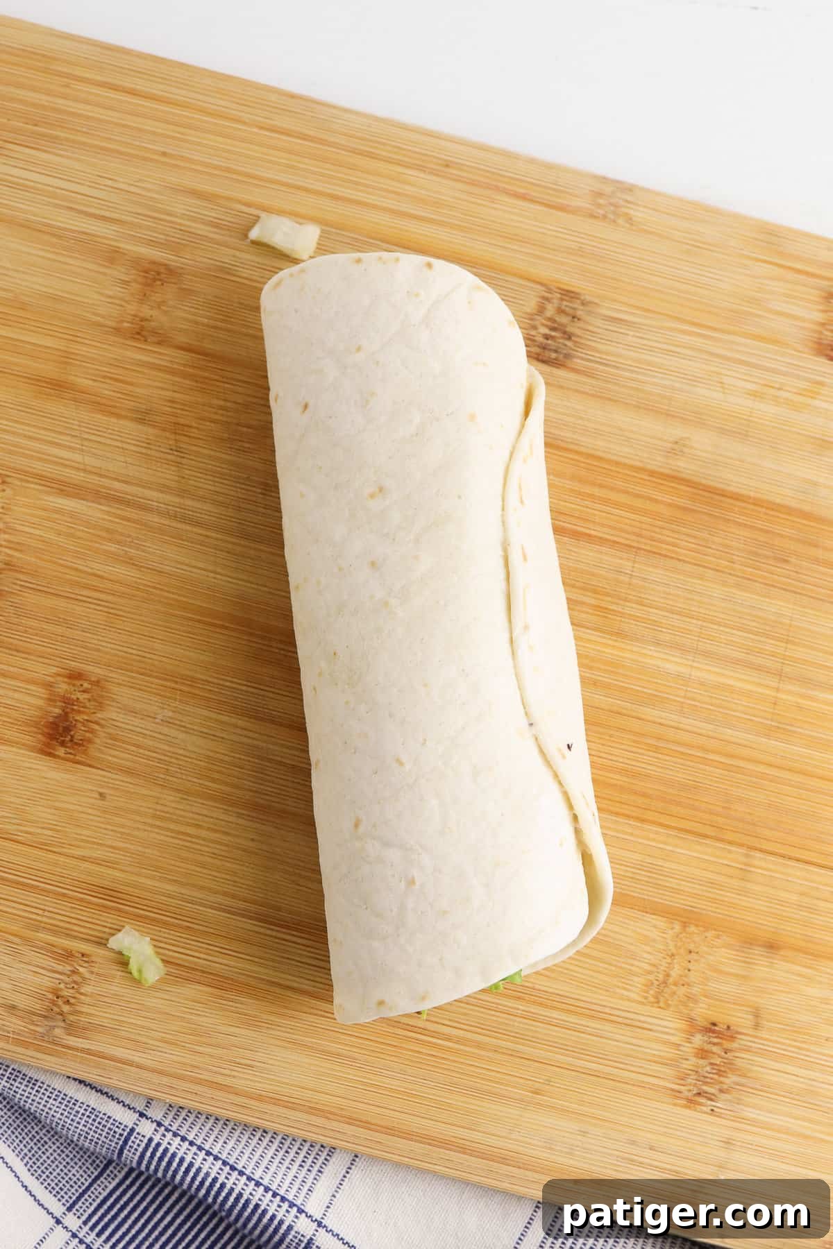 Tortillas wrapped into a log, similar to a burrito. The tightly rolled tortilla, filled with BLT ingredients and ranch dressing, is secured in plastic wrap, ready for chilling.