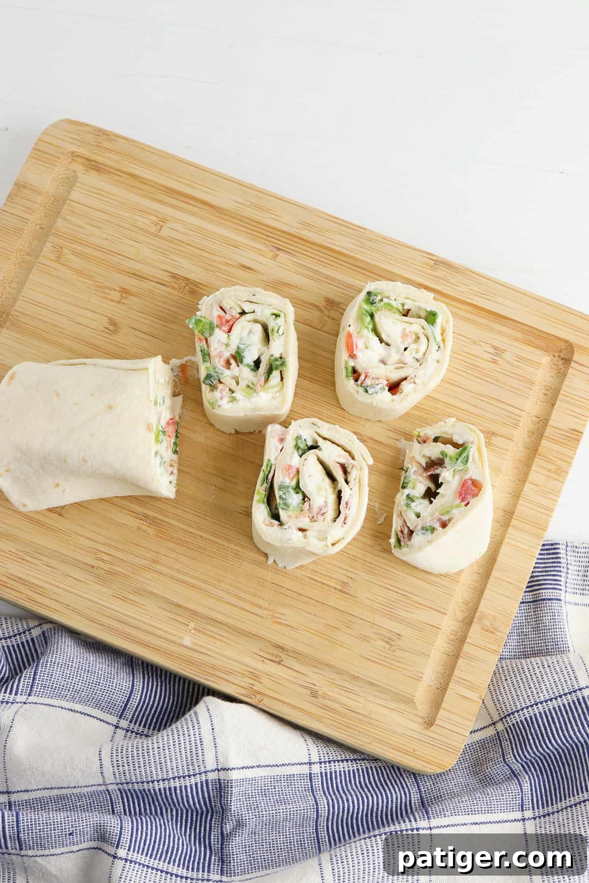 Rolled up tortilla being cut into 1-inch slices on a wooden cutting board. A sharp serrated knife is used to create perfectly formed BLT pinwheels, showcasing the layers of filling.