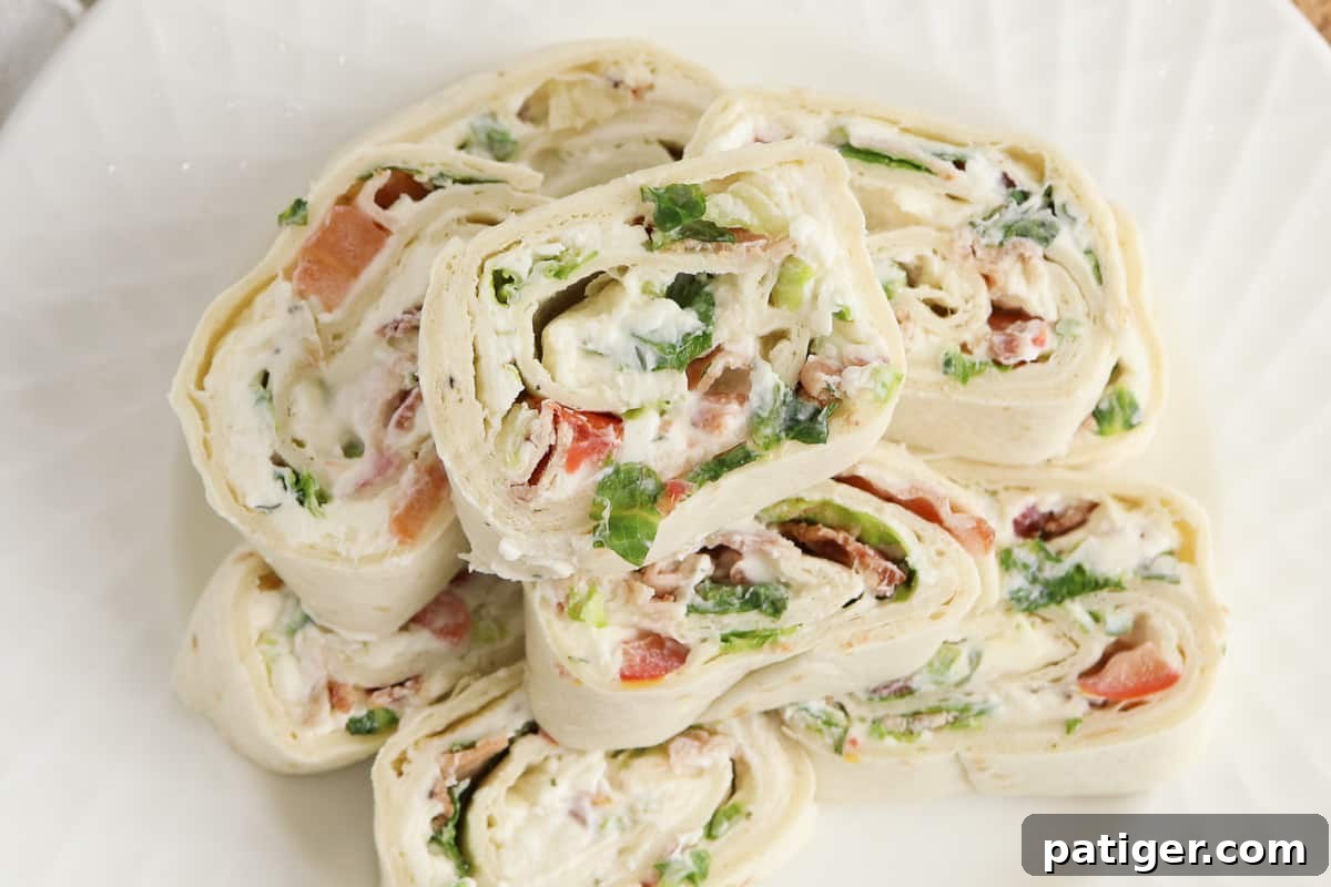 Top-down view of ranch pinwheels stacked on a white plate, garnished with fresh parsley. These neatly arranged BLT roll-ups are a perfect visual representation of a delicious and easy appetizer.