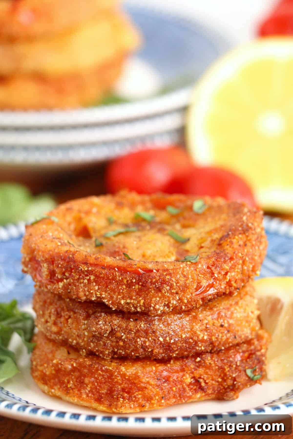Golden crispy fried tomatoes with lettuce, tomatoes, and lemon wedge in background.
