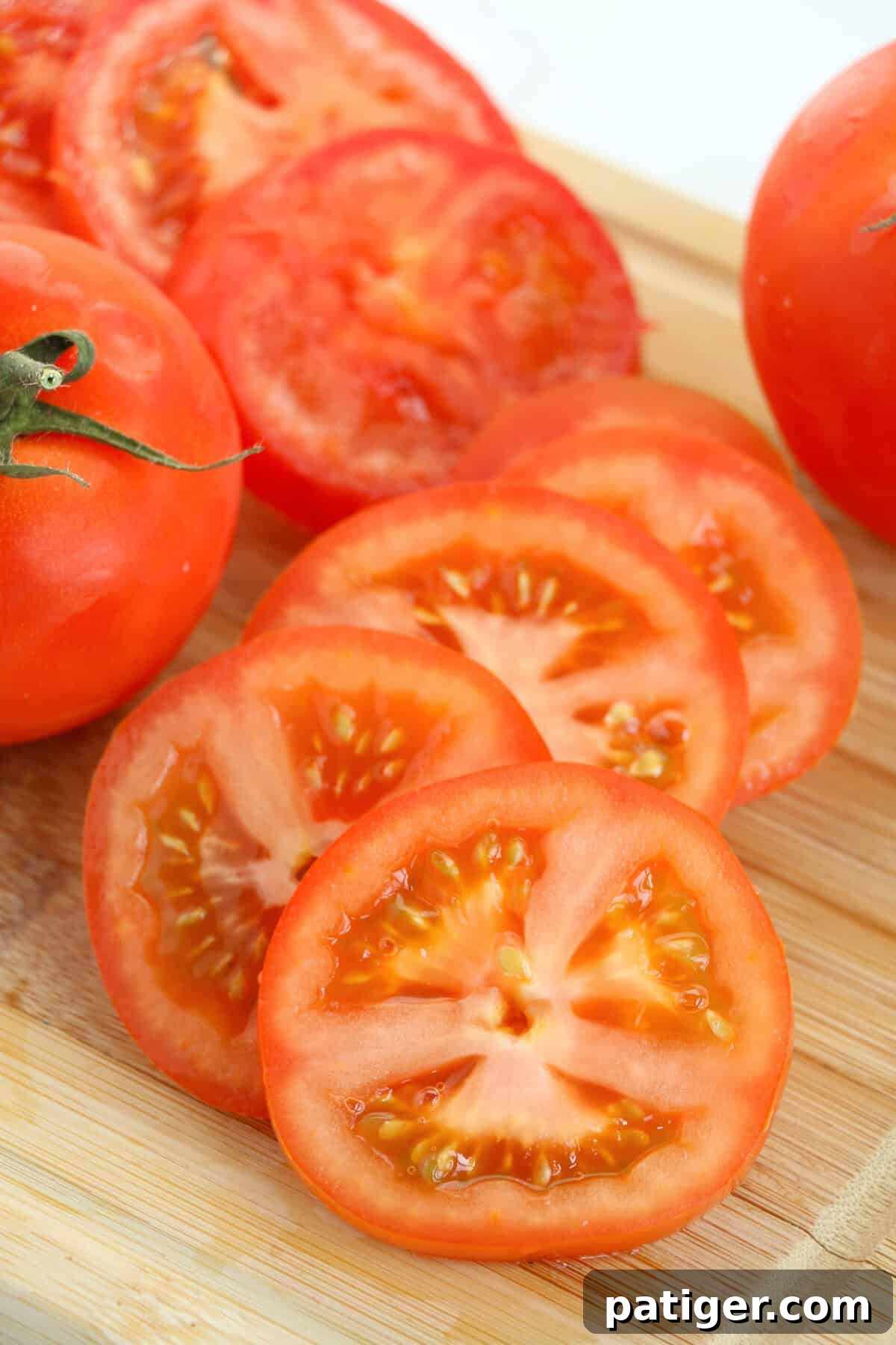 Red tomato sliced thick on a wooden cutting board.