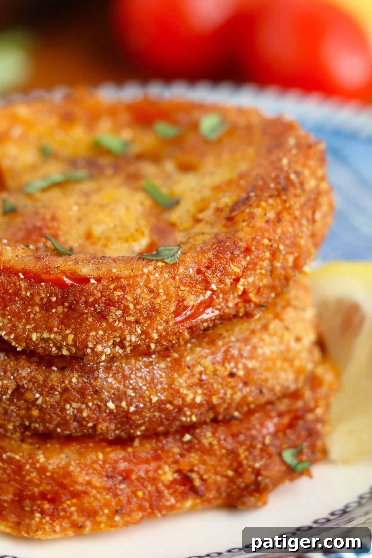 Crispy fried red tomatoes garnished with basil and stacked on a plate for serving.