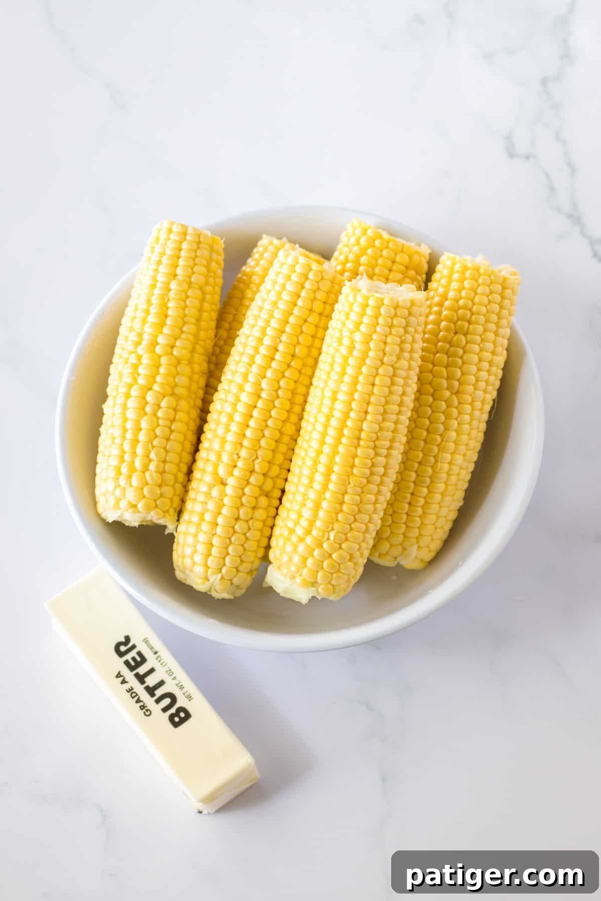 Set It and Forget It Corn on the Cob 4 Fresh corn on the cob resting next to a stick of creamy butter, essential ingredients for this recipe.
