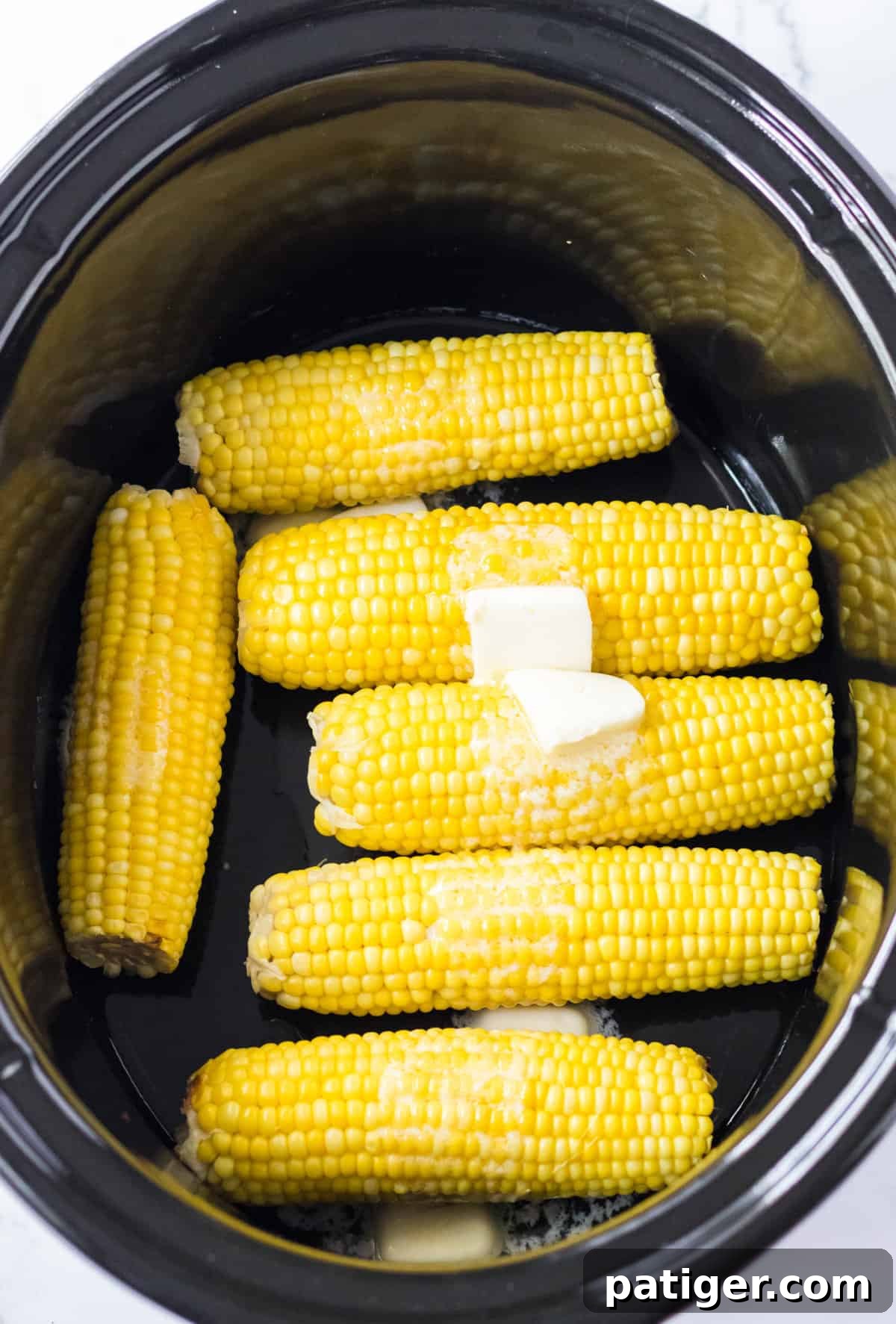Set It and Forget It Corn on the Cob 6 Butter melting gracefully on top of the cooked corn cobs inside the crockpot.