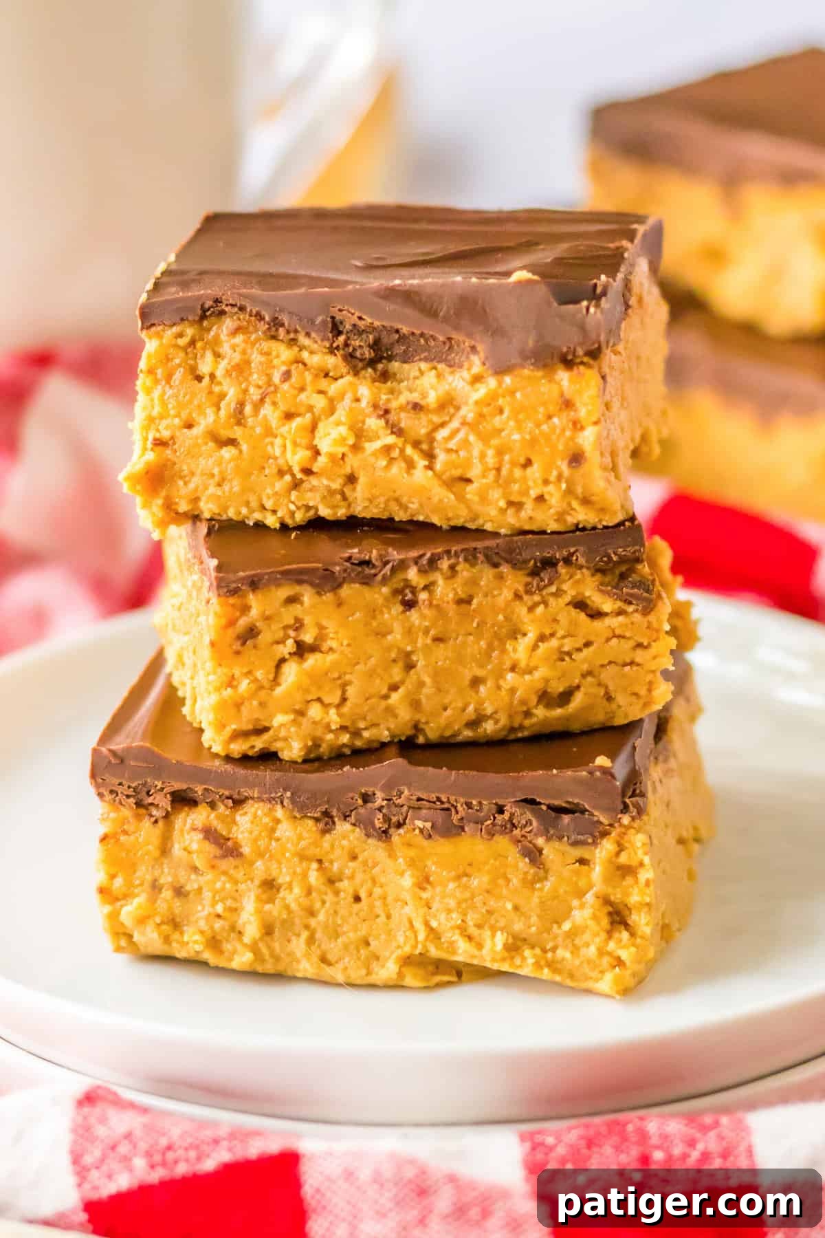 Chilled Chocolate Peanut Butter Fudge Squares 2 Stacked 5-ingredient no-bake chocolate peanut butter bars on a white plate, showcasing their rich layers.