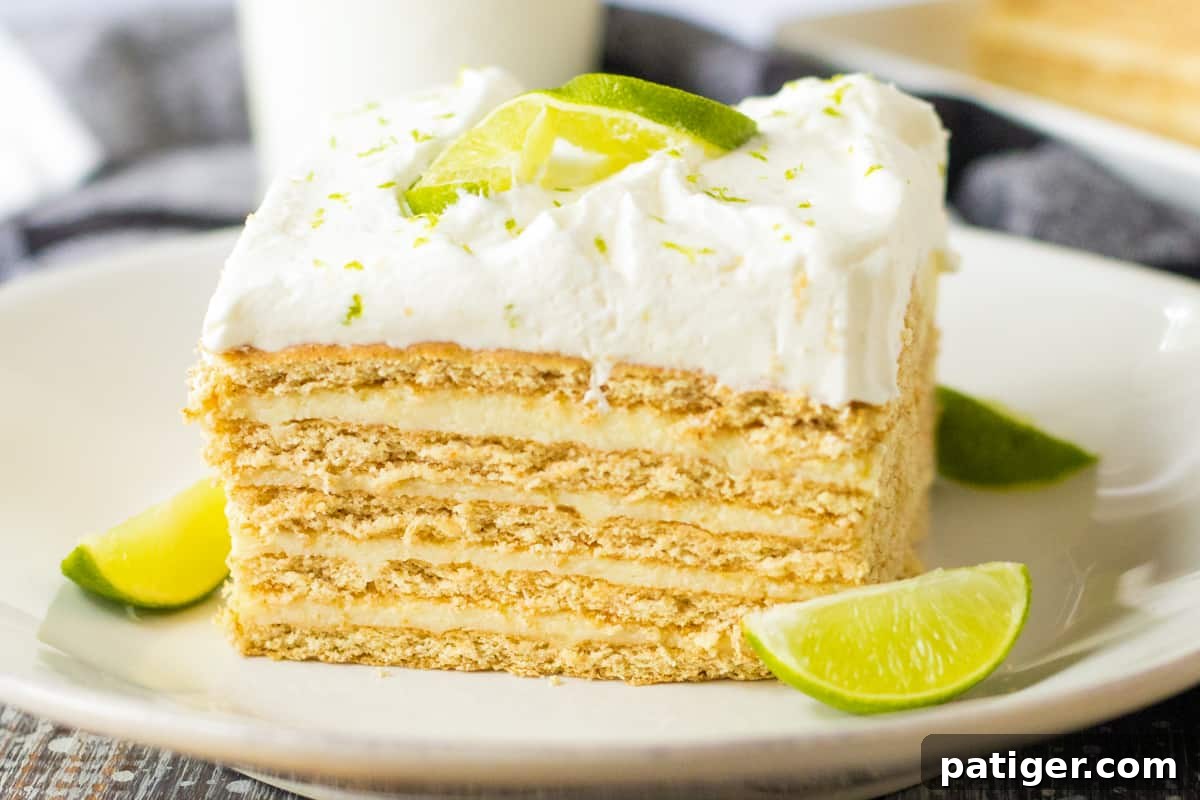 Square slice of key lime icebox cake with layers of key lime custard and graham crackers topped with whipped cream and garnished with key lime slice.
