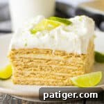 Slice of key lime icebox cake with layers of key lime custard and graham crackers on white plate garnished with slice of key lime.