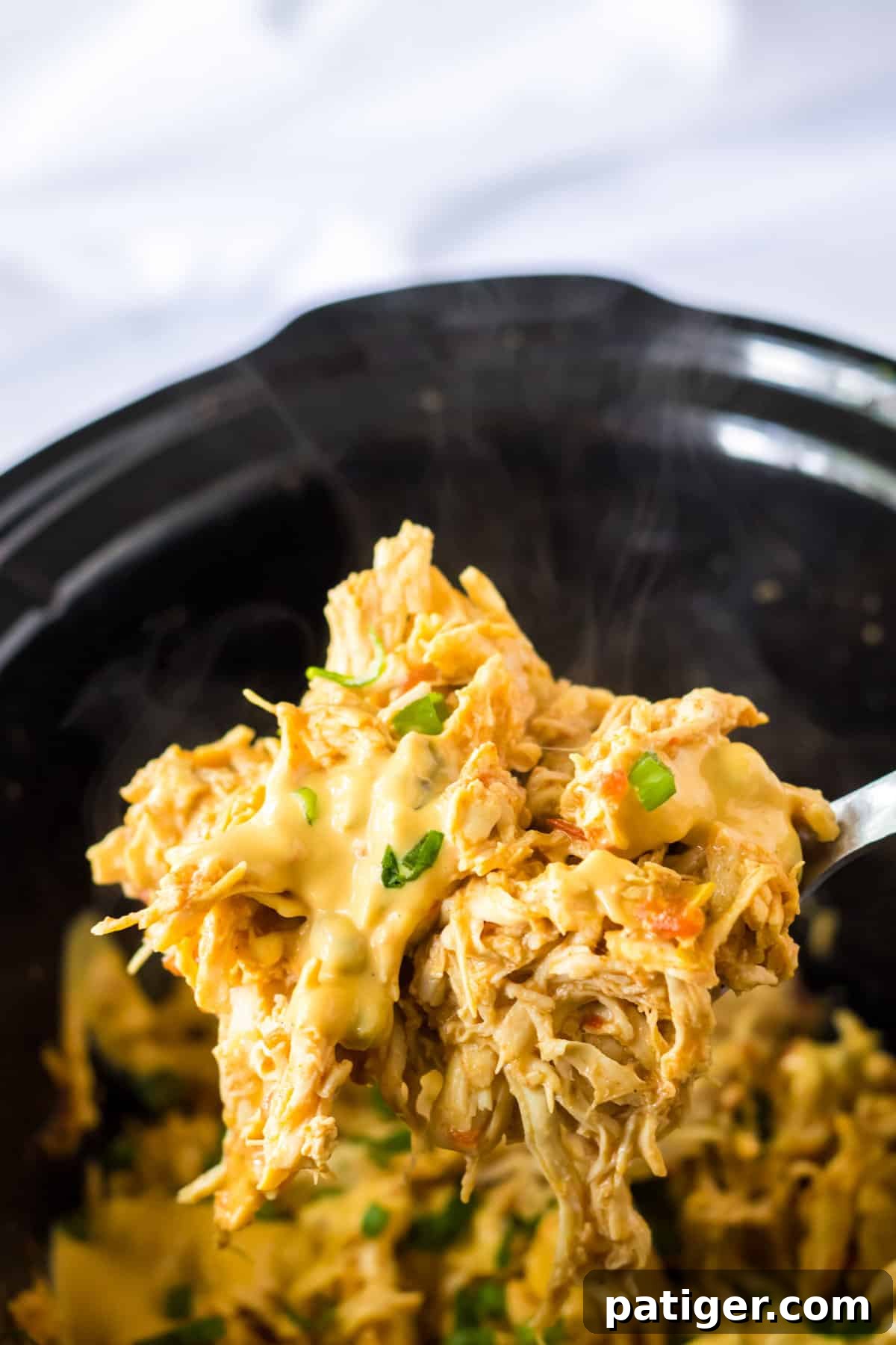 A spoon generously scooping delicious, cheesy queso chicken out of the slow cooker, highlighting its rich and creamy texture.
