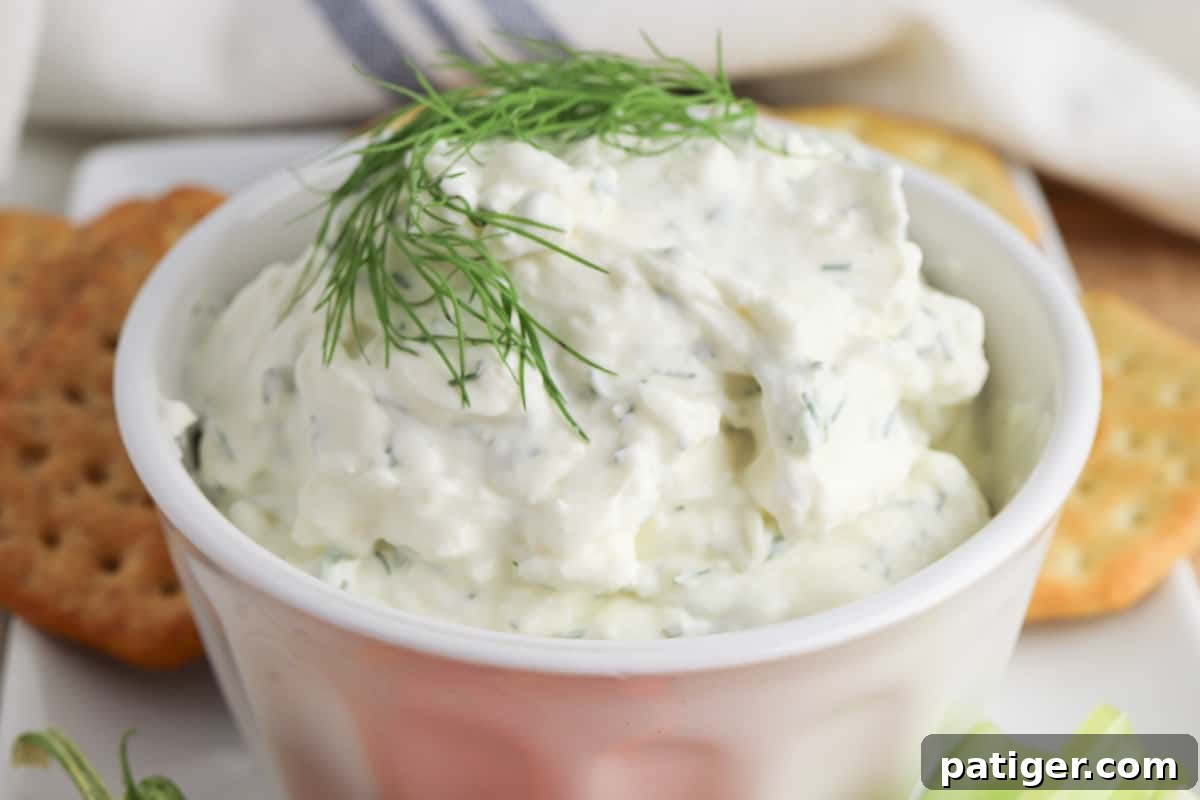 Zesty Dill Cream Cheese Dip 7 Creamy dill dip garnished with a sprig of fresh dill and served in a bowl with crackers for dipping.