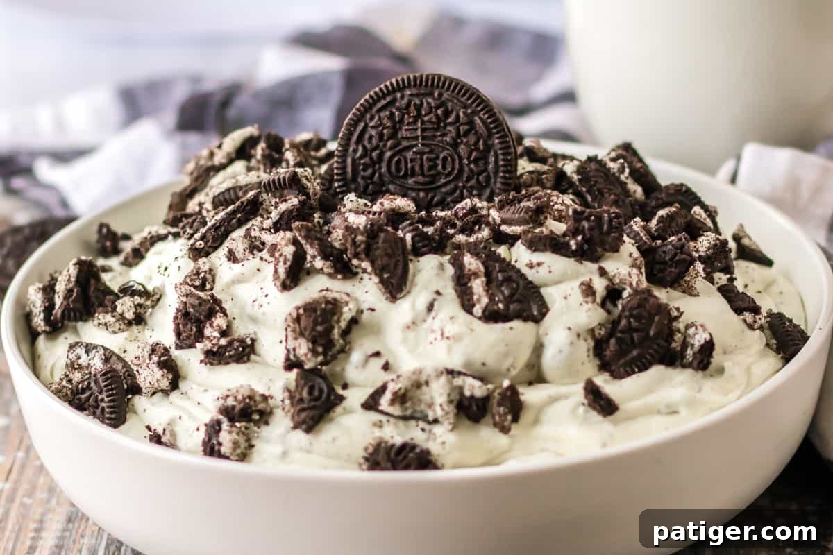 A glass bowl of creamy Oreo cookie fluff served with a glass of milk in the background.