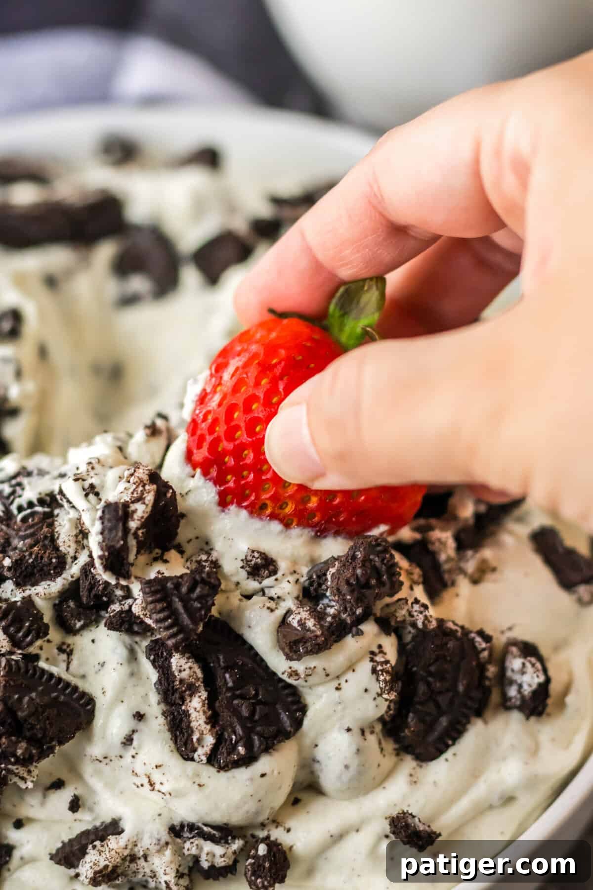 A fresh, ripe strawberry being dipped into a bowl of creamy Oreo Fluff dessert.