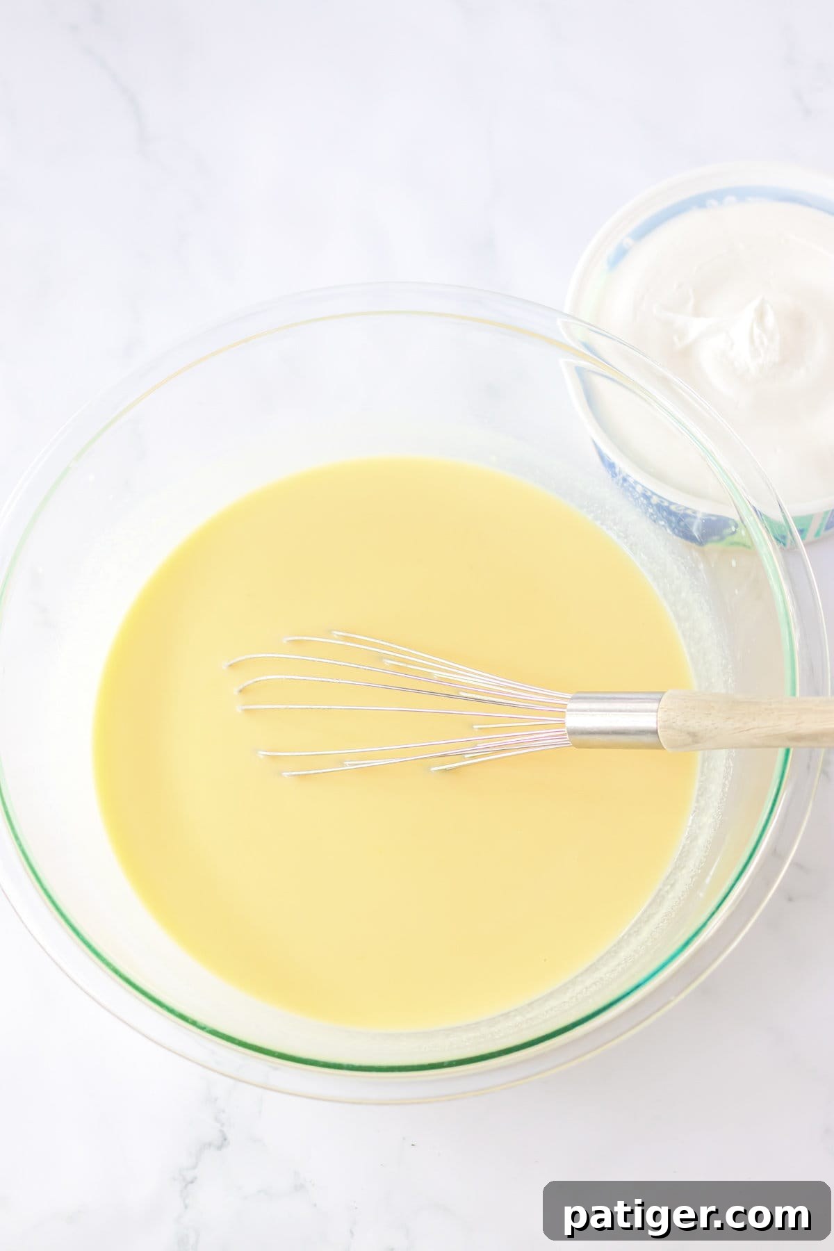 Glass mixing bowl containing whisked vanilla pudding mix with milk, forming a smooth base for Oreo Fluff.