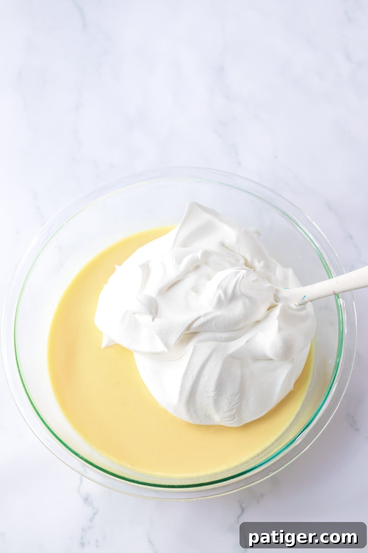 Thawed Cool Whip being gently folded into the vanilla pudding mixture in a glass mixing bowl for Oreo Fluff.