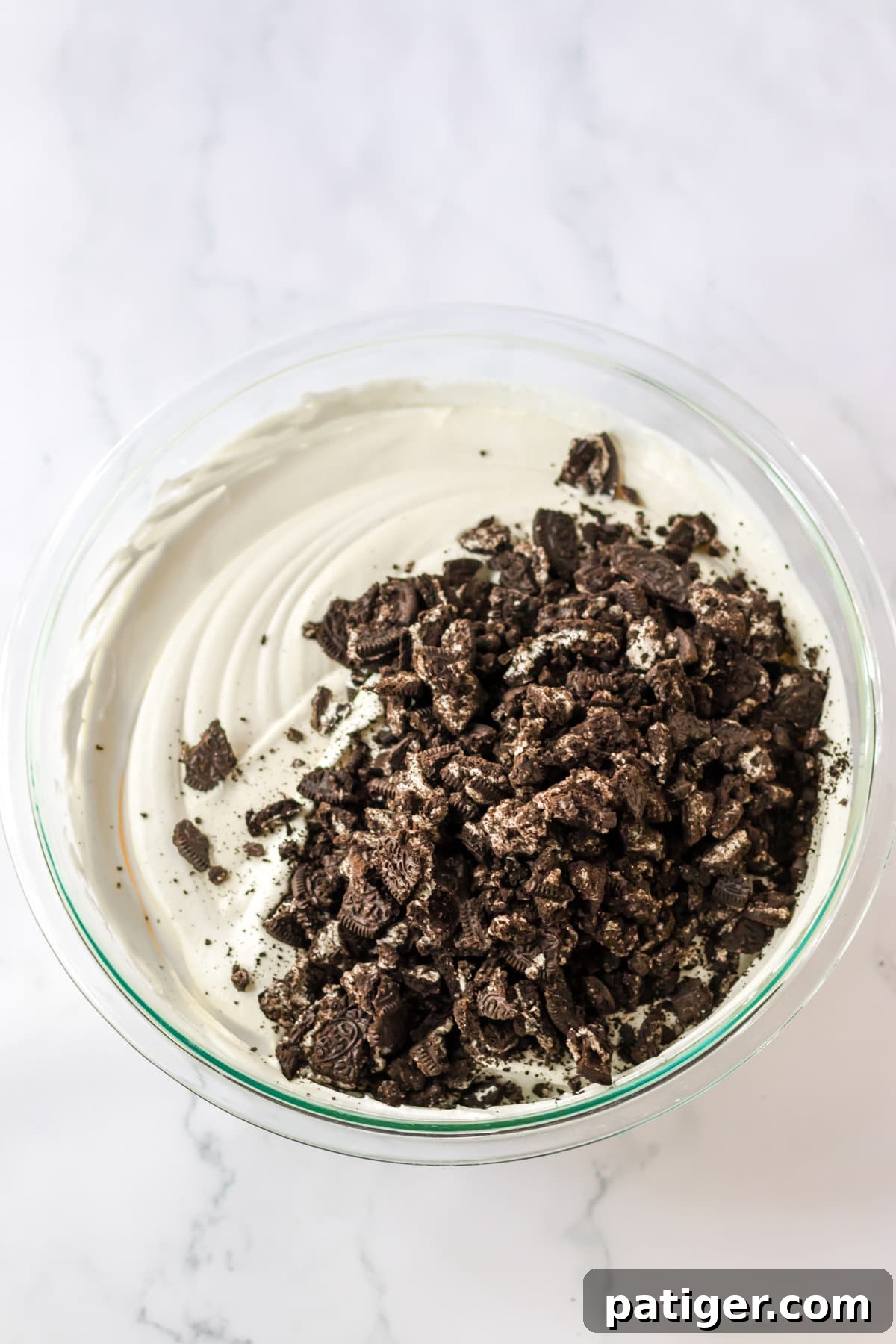 Crushed Oreo cookies being gently folded into the creamy pudding and Cool Whip mixture in a mixing bowl for Oreo Fluff.