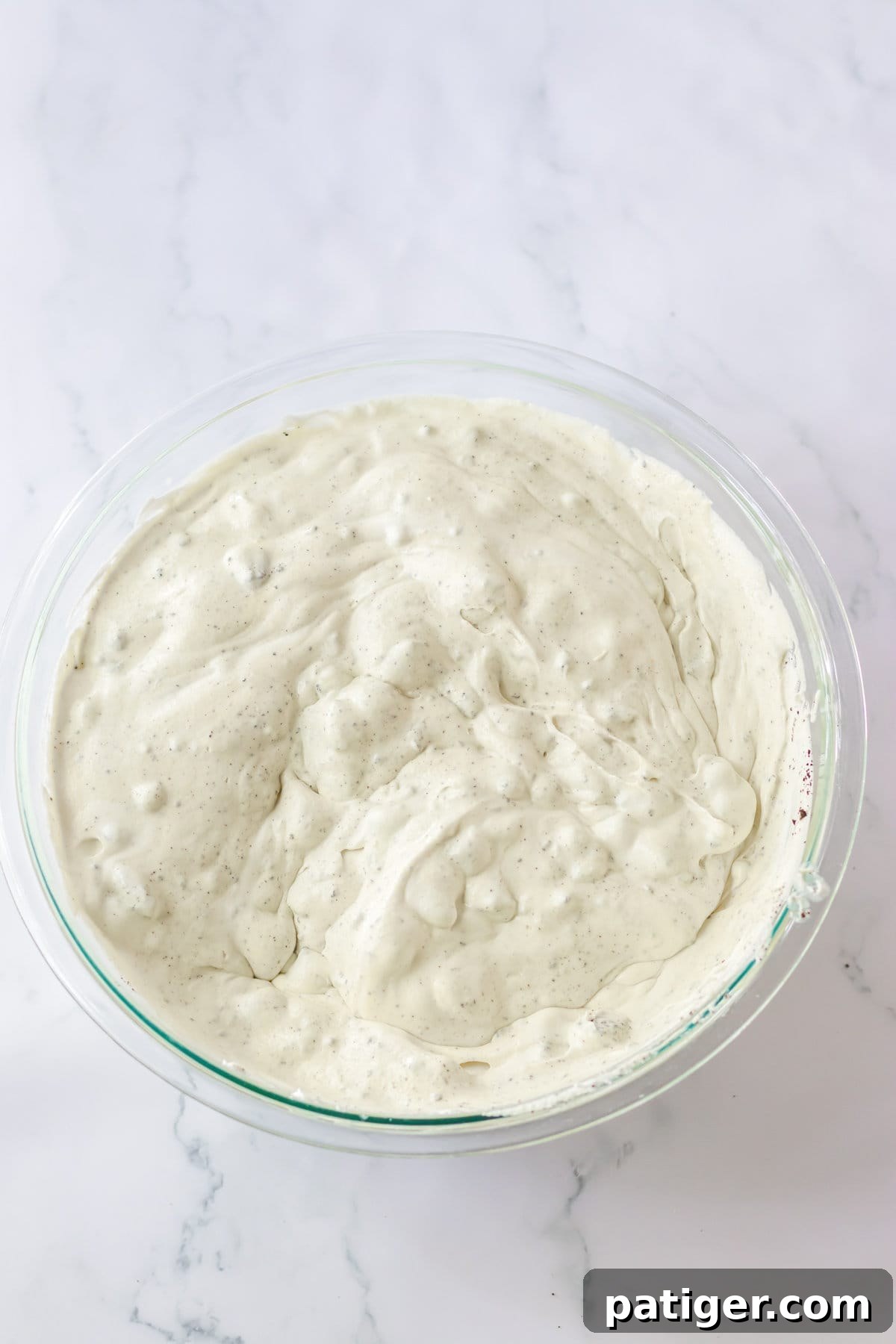 Oreo cookie fluff dessert covered with plastic wrap, chilling in a glass mixing bowl.
