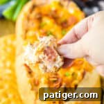 Hand holding a ritz cracker dipped in creamy mississippi sin dip with bacon.