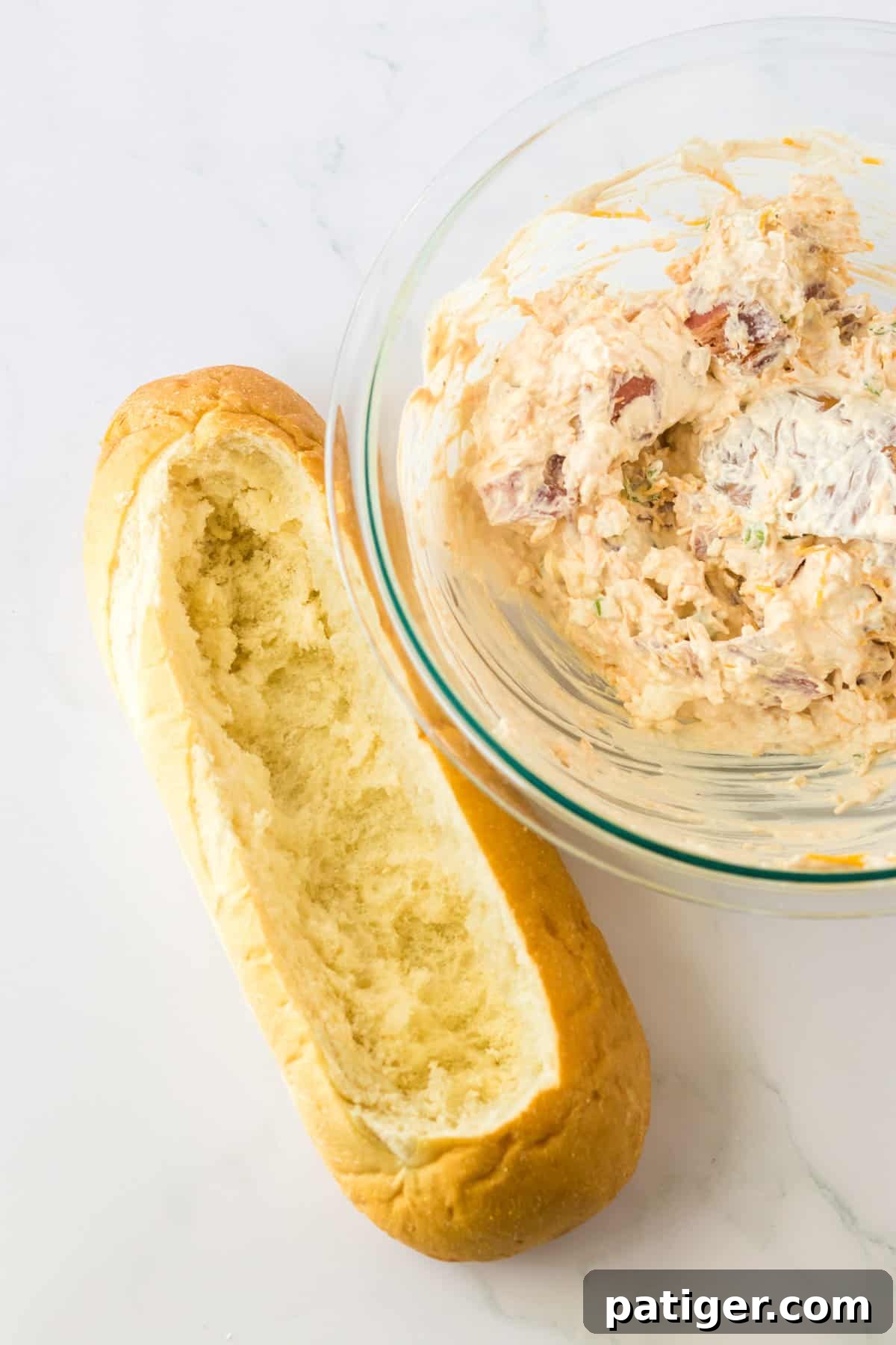 Hollowed out loaf of bread with bowl of bacon cheese dip next to it.