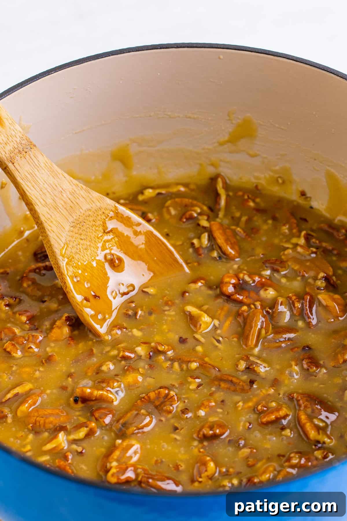Wooden spoon in the pecan praline mixture in a blue dutch oven.