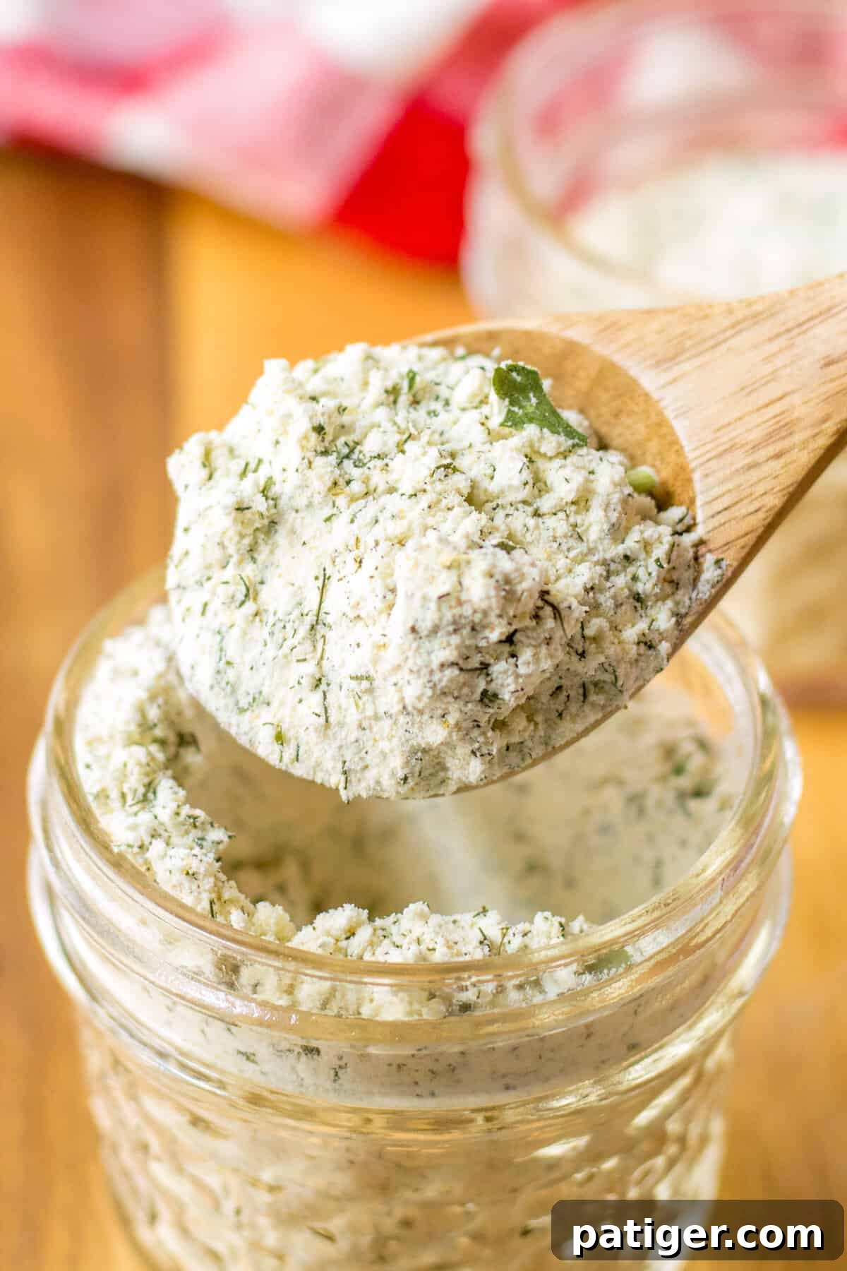 Delicious Homemade Ranch Seasoning 5 A small wooden spoon carefully lifting a portion of homemade ranch seasoning mix out of a glass jar, highlighting its texture and freshness.