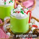 Slow cooker green grinch hot chocolate in a glass mug with whipped cream, mini marshmallows, christmas sprinkles, and candy canes.