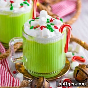 Slow cooker green grinch hot chocolate in a glass mug with whipped cream, mini marshmallows, christmas sprinkles, and candy canes.