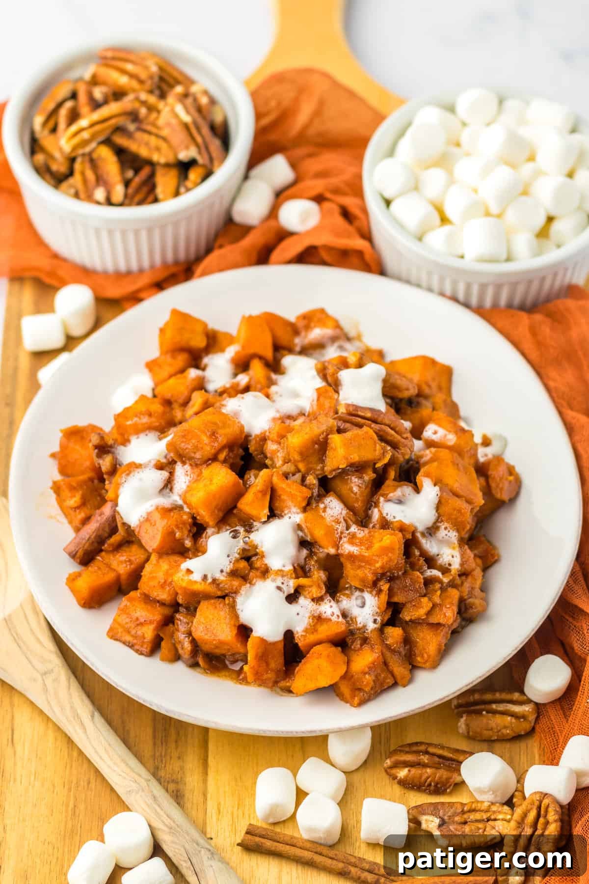 Slow Cooker Sweet Potato Bliss 2 Slow cooker sweet potatoes served on a white plate with additional pecans and mini marshmallows surrounding it, showcasing the golden-brown topping.
