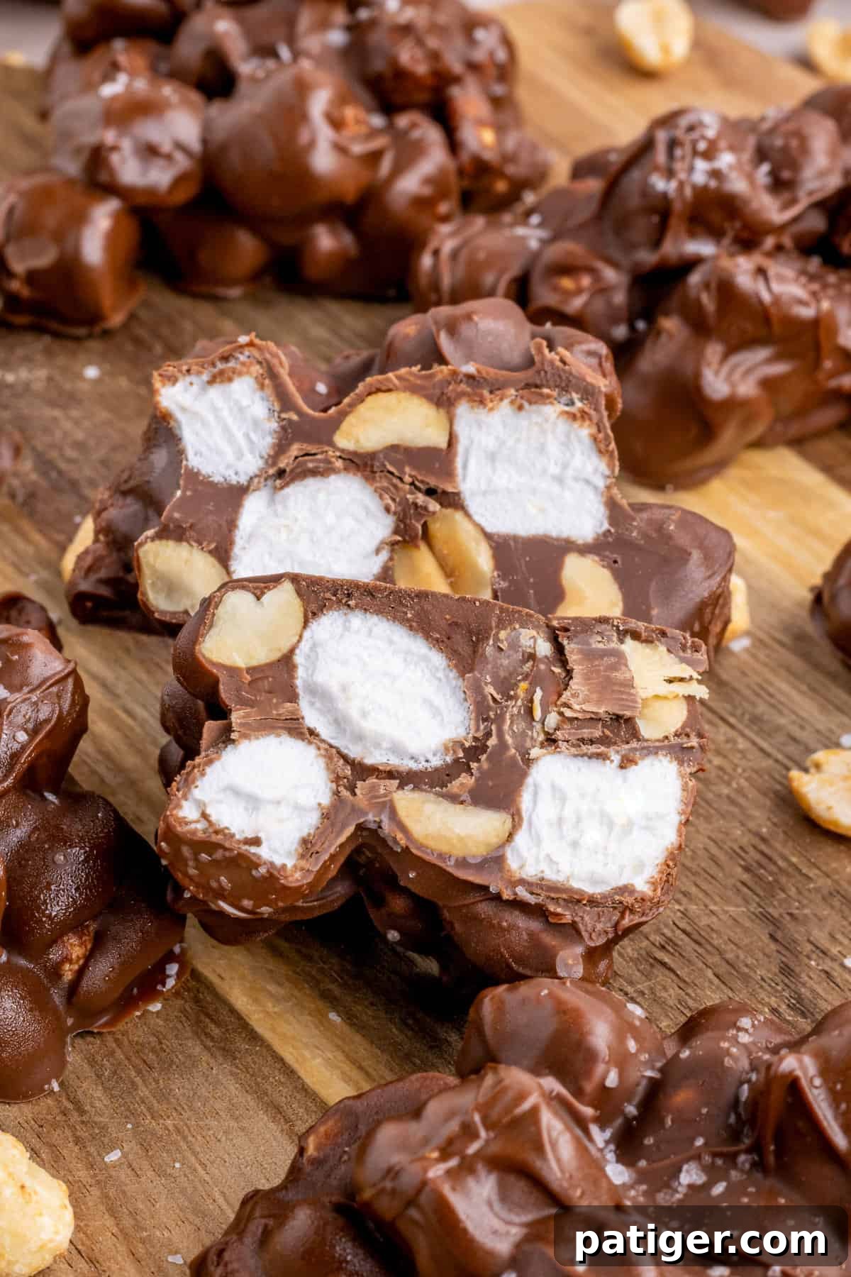 Rocky road candy on cutting board with one cut in half to show the marshmallows and peanuts inside in the chocolate clusters. 