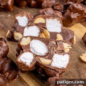 Rocky road candy on cutting board with one cut in half to show the marshmallows and peanuts inside in the chocolate clusters.