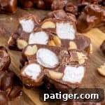 Rocky road candy on cutting board with one cut in half to show the marshmallows and peanuts inside in the chocolate clusters.