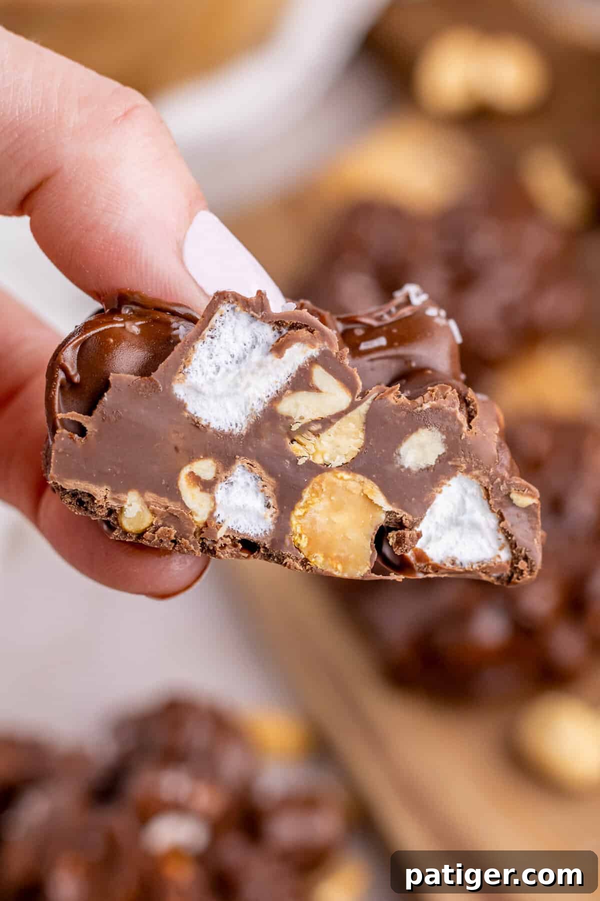 Hand holding piece of rocky road chocolate cut in half to show marshmallows and peanuts inside.