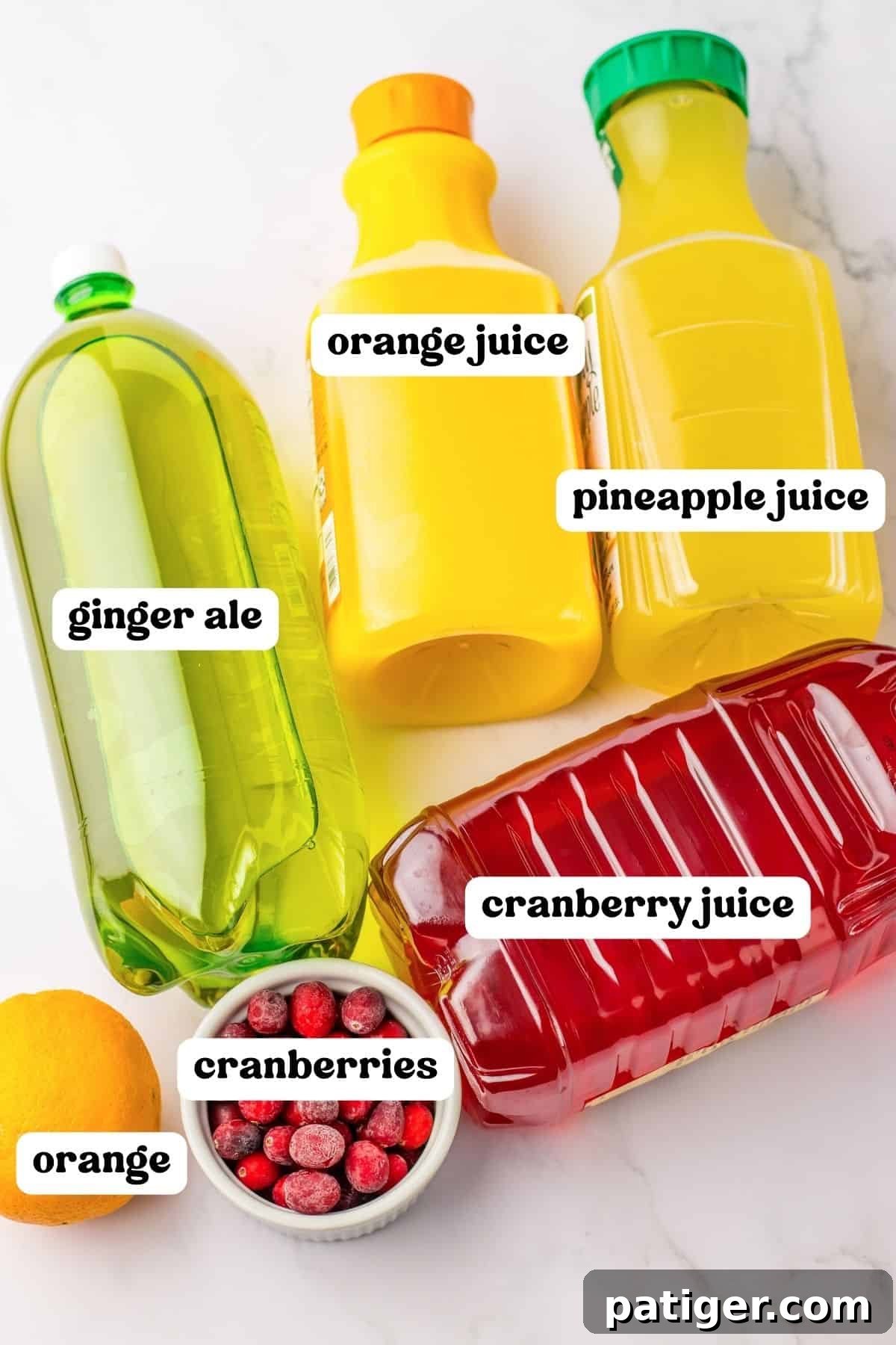Bottles of cranberry cocktail, pineapple juice, orange juice, and ginger ale, along with fresh cranberries and an orange, laid out for the Christmas punch recipe.