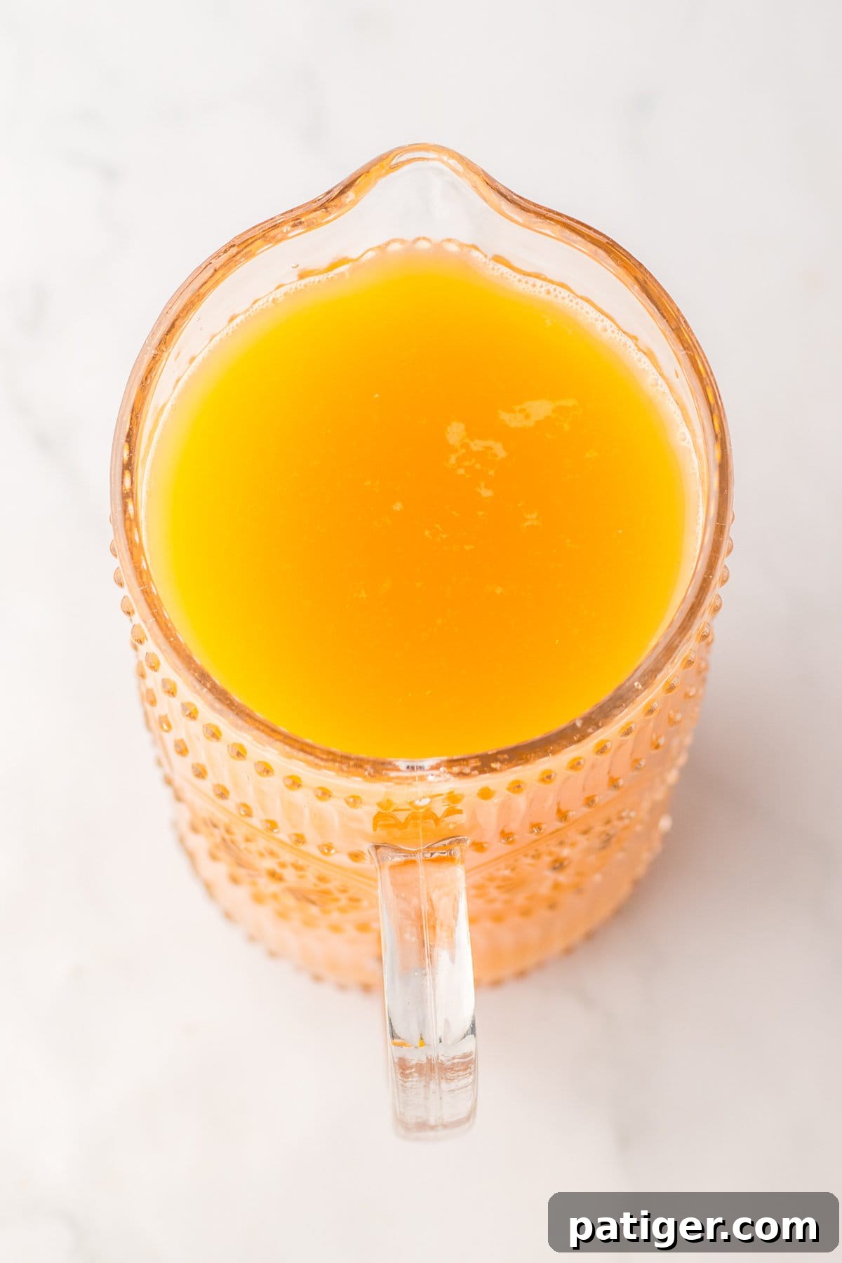A glass pitcher filled with a vibrant orange-hued punch, freshly mixed and ready for garnishing.