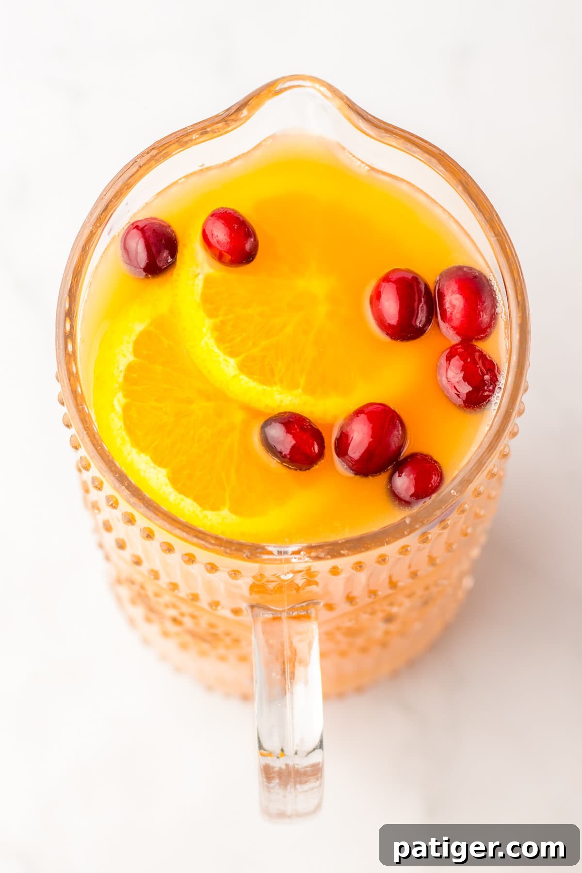 A pitcher of non-alcoholic holiday punch, now enhanced with colorful fresh cranberries and bright orange slices, ready to chill.