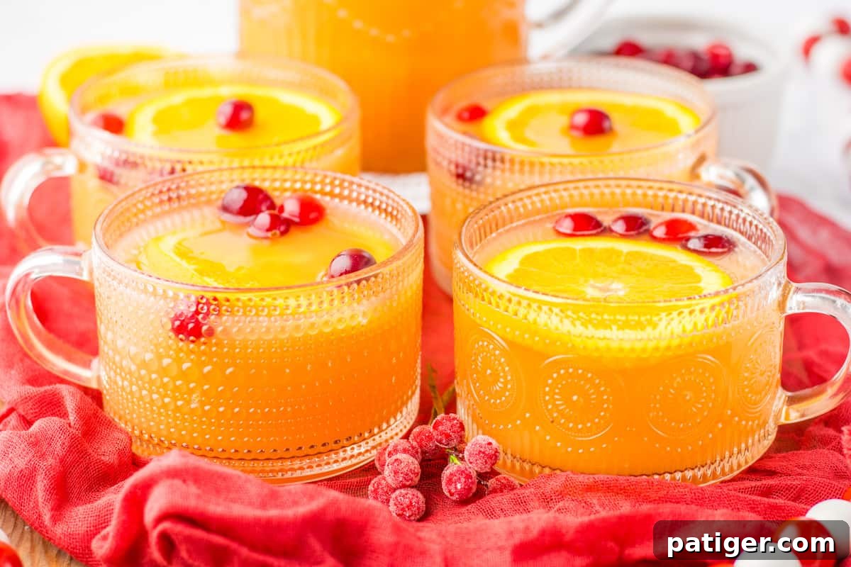 Four glass mugs filled with festive non-alcoholic Christmas punch, each garnished with vibrant orange slices and plump cranberries, ready to be enjoyed.