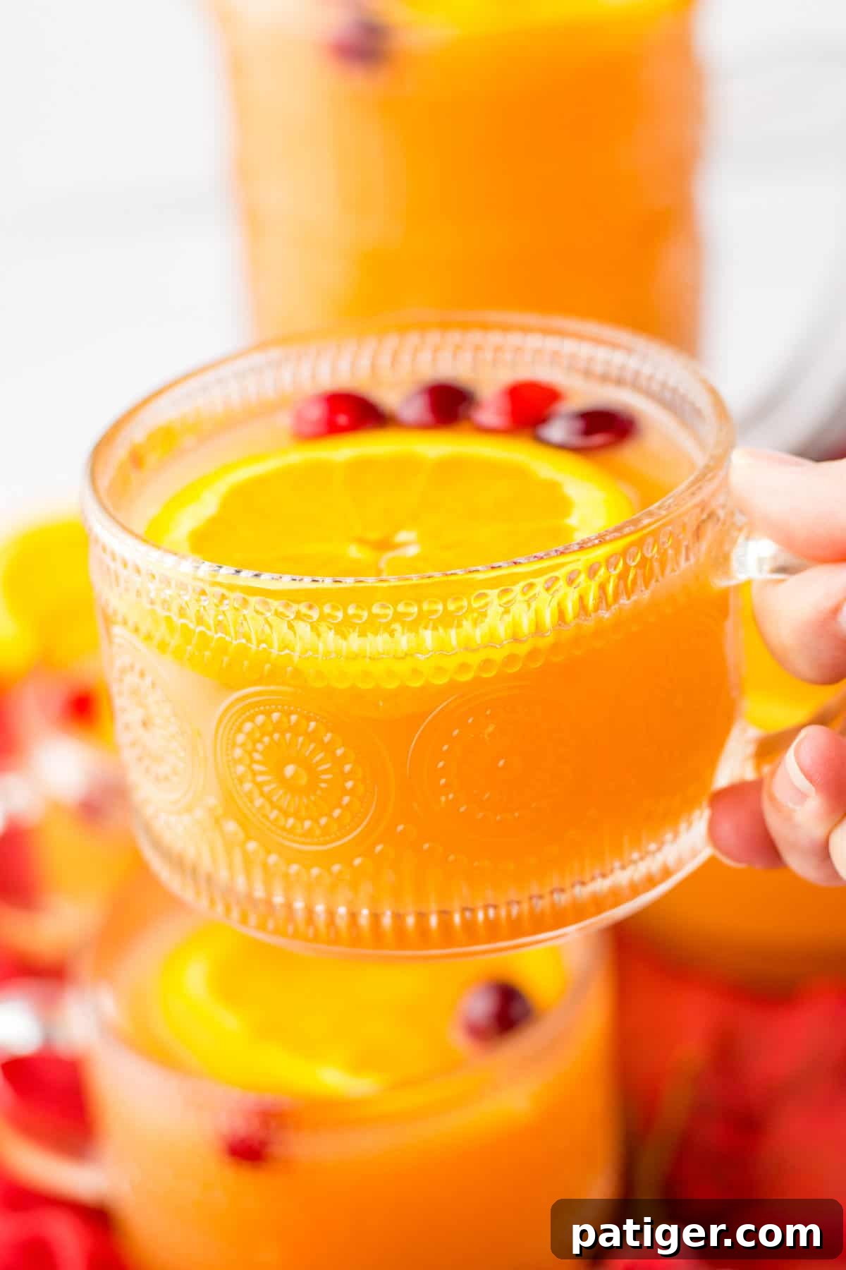 A hand holding a glass of vibrant Christmas brunch punch, showcasing its festive color and garnishes, perfect for holiday celebrations.