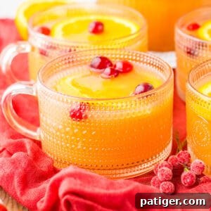 A close-up of a glass mug filled with Christmas morning punch, adorned with fresh cranberries and an orange slice, radiating holiday cheer.