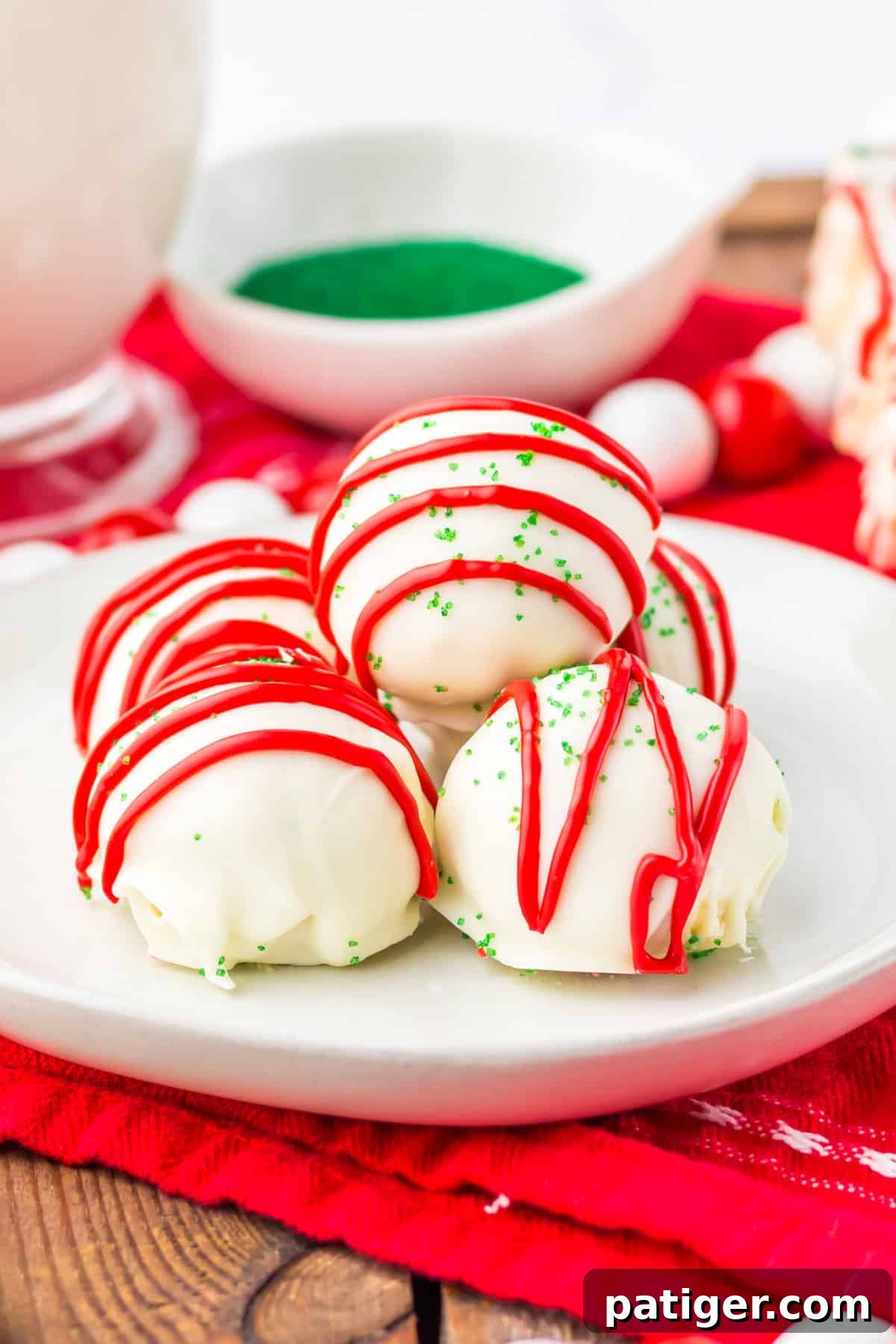 Little Debbie Christmas Tree Cake Balls on a white plate, adorned with green sanding sugar and red icing drizzles, with a glass of milk in the background.