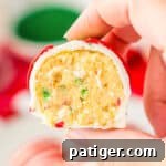 Hand holding Little Debbie Christmas Tree Cake Ball cut in half to reveal vanilla cake center with dots of red and green sprinkles.