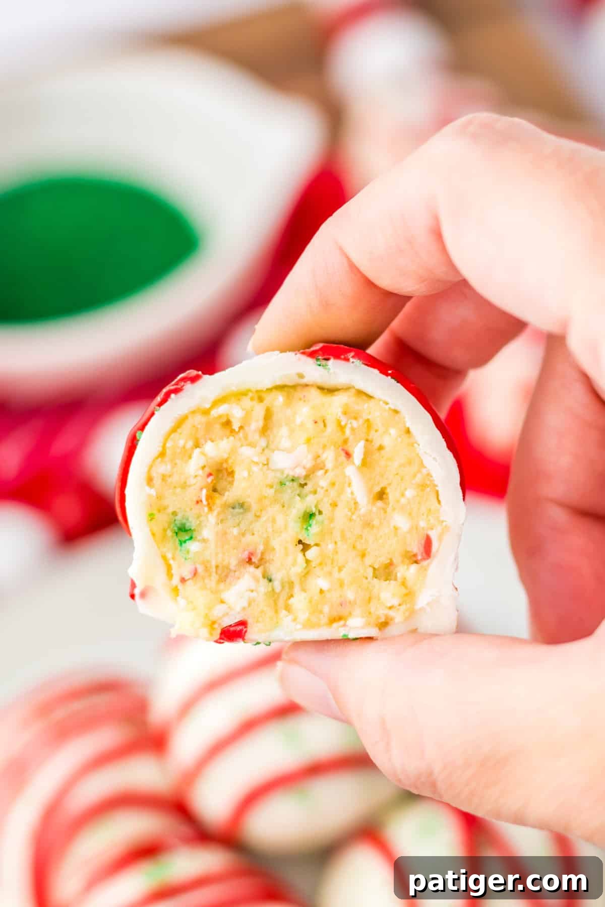 A hand holding a Little Debbie Christmas Tree Cake Truffle, cut in half to showcase its soft cake interior speckled with red and green sprinkles.