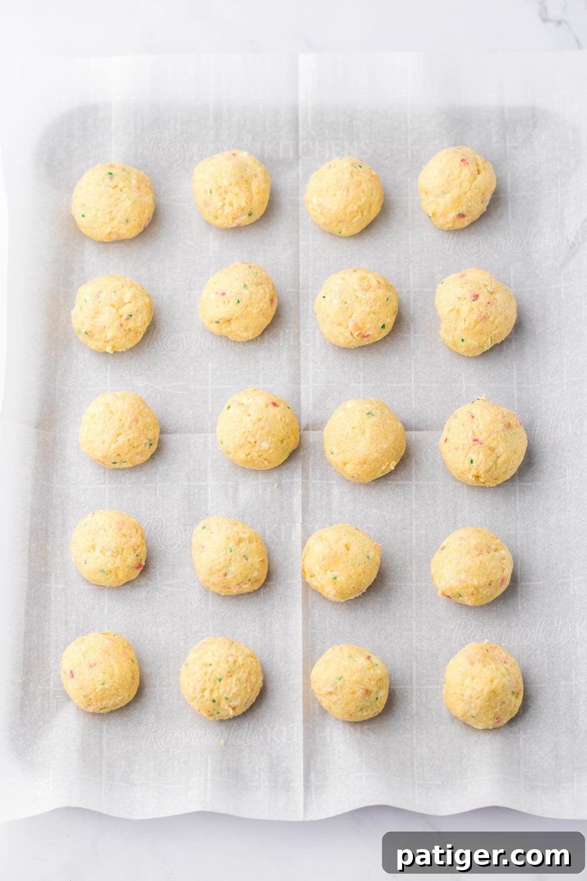 Uniform 1-inch dough balls made from Christmas Tree Cakes and cream cheese, arranged neatly on a parchment-lined baking sheet.