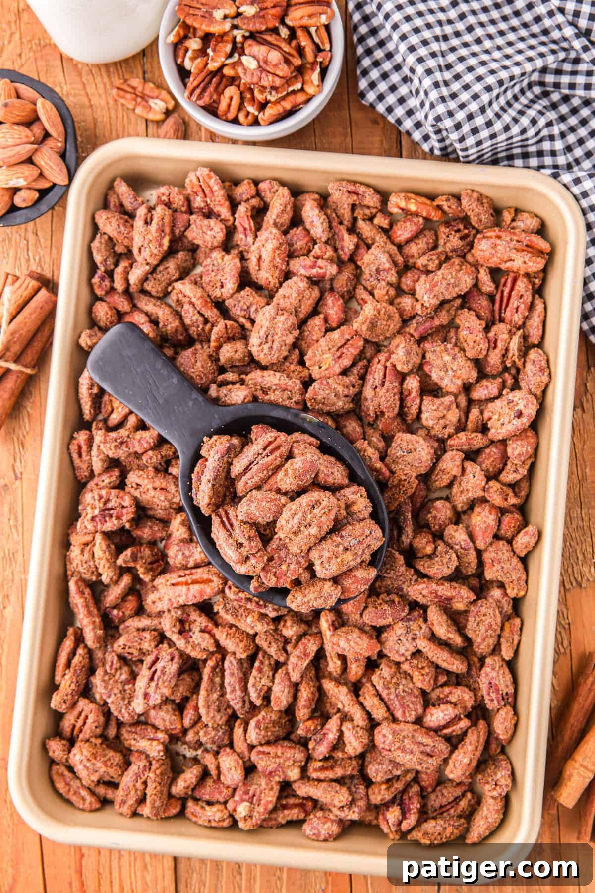 Candied almonds and pecans cooling on a backing sheet with a small black scoop nearby.