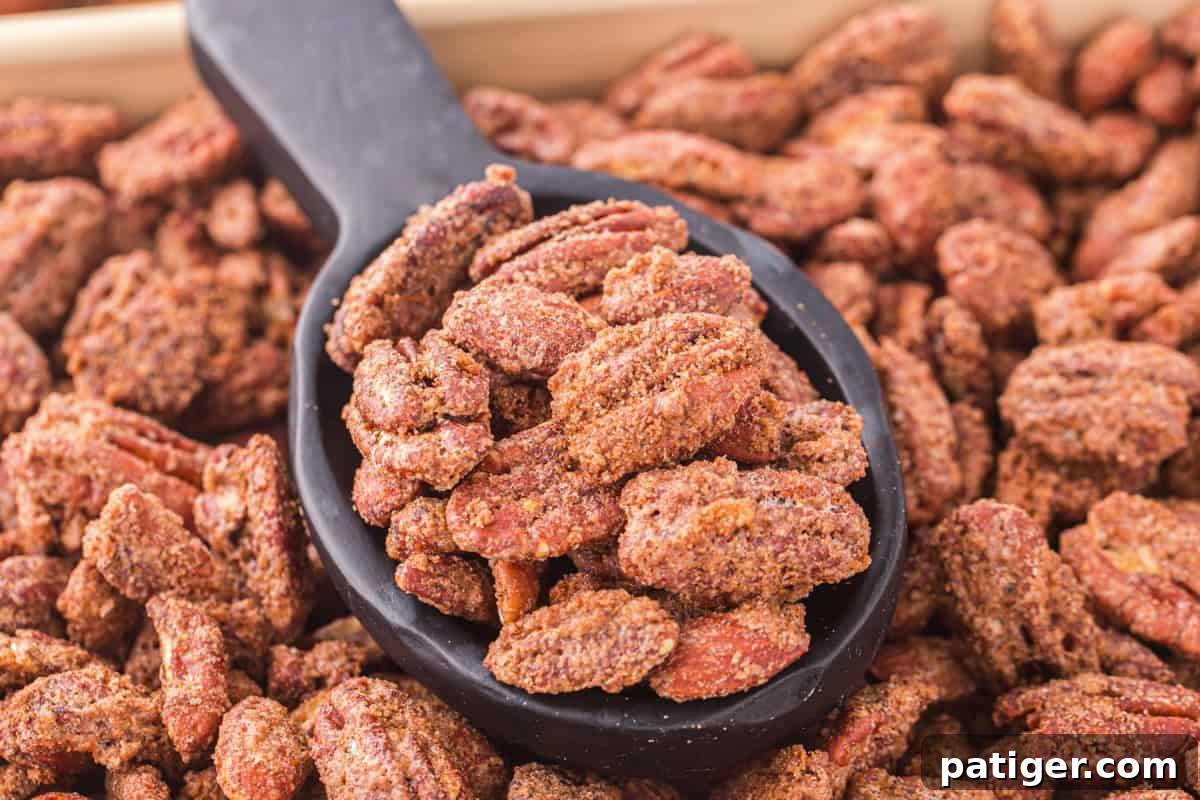 Cinnamon almonds and pecans on a sheet pan with some scooped into a black spoon, showcasing their appealing glaze.